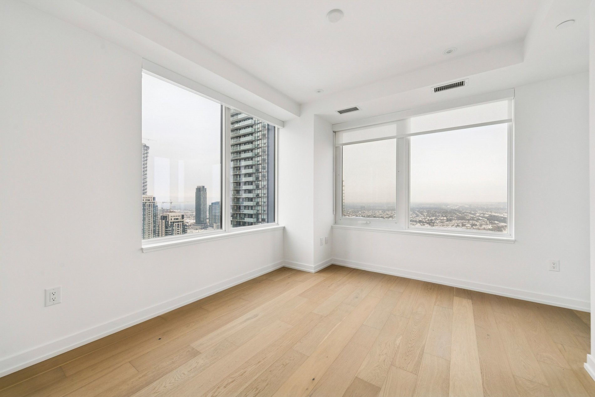 Bright corner bedroom with floor-to-ceiling windows and city views